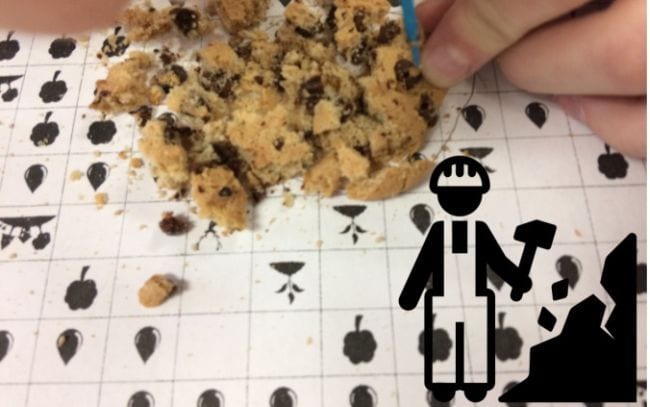 Student's hand digging through a crumbled cookie to pull out chocolate chips